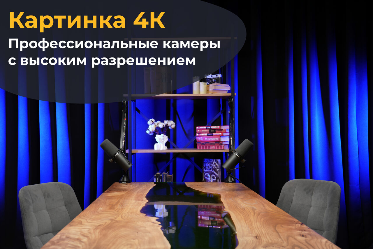 Арендовать Лофт Восторг. Современное офисное пространство с деревянным столом, двумя серыми стульями и полкой, на которой стоят книги и декор. Сзади темно-синие занавески. Использовано направленное освещение. Текст на изображении: "Картинка 4К, Профессиональные камеры с высоким разрешением".