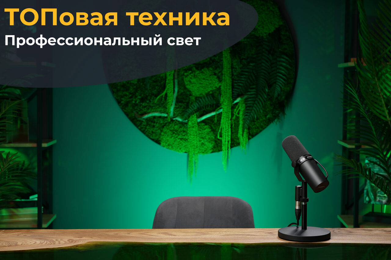 Арендовать Лофт Восторг. Общий вид стола с деревянной поверхностью, на котором стоит микрофон. За стулом серая обивка. На стене зелёная растительность в круглом панно. Слева видна полка с растениями. Освещение зелёного цвета. Текст: "ТОПовая техника. Профессиональный свет".