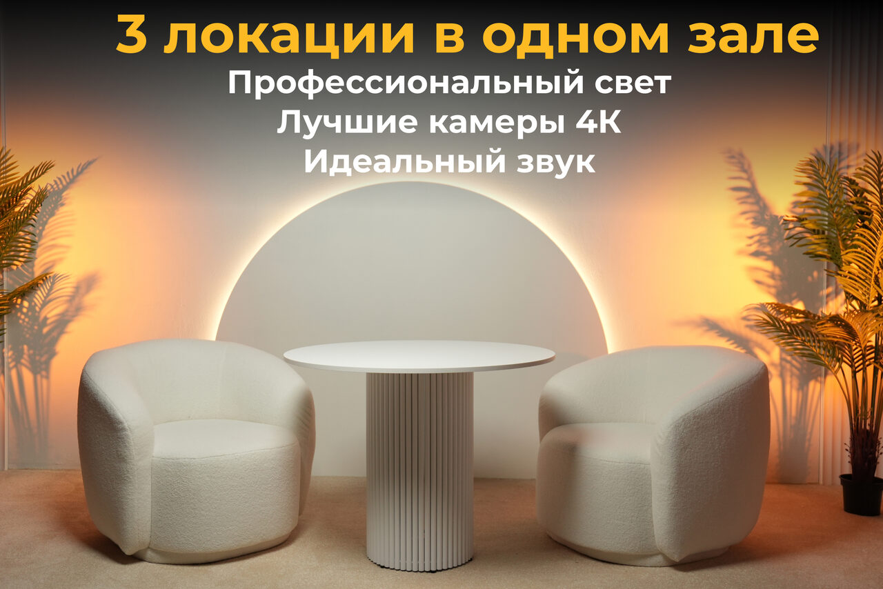 Арендовать Лофт Восторг. Современное помещение с двумя белыми креслами и круглым столом на фоне круглого светящегося элемента. Слева и справа от мебели пальмы в горшках. Текст на изображении: "3 локации в одном зале. Профессиональный свет, Лучшие камеры 4К, Идеальный звук."