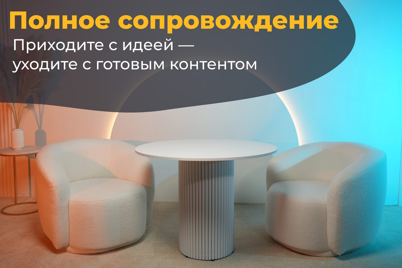 Арендовать Лофт Восторг. Современное пространство с двумя белыми креслами и круглым столом с ребристой ножкой. На фоне световая арка с голубым и оранжевым свечением. Слева на столике бежевые вазы. Текст: «Полное сопровождение. Приходите с идеей — уходите с готовым контентом».