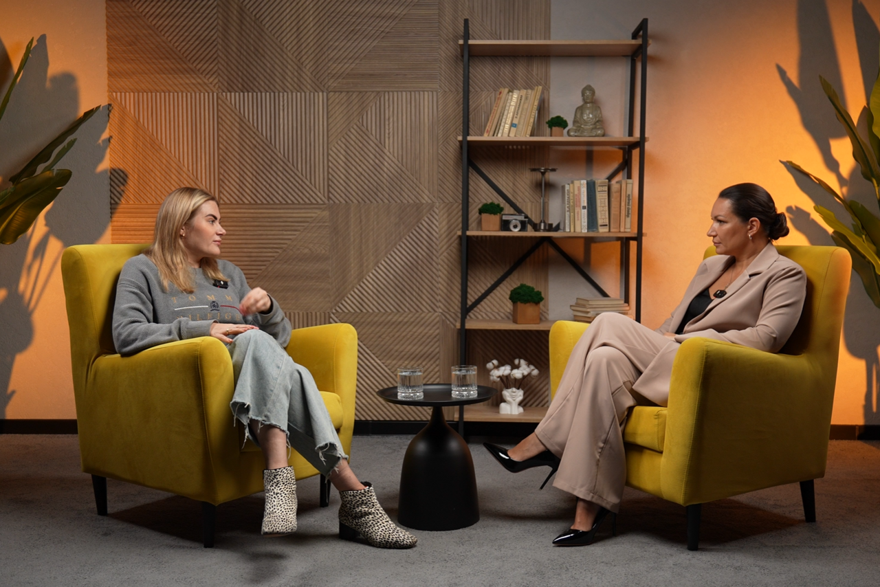 Арендовать Лофт  Эйфория. Пространство для встречи с двумя желтыми креслами, круглый черный столик с двумя стаканами, книжная полка с книгами и декором. Стена с геометрическим деревянным узором. Освещение теплое. Напольное покрытие серое.