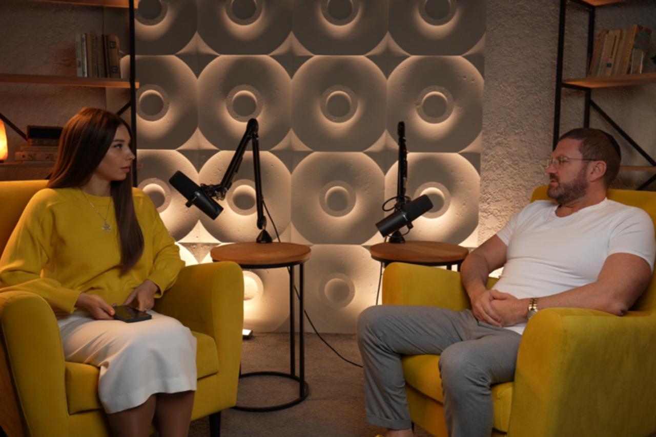 Арендовать Лофт  Эйфория. Пространство для подкаста, два желтых кресла, круглые столики с микрофонами, светло-серые объемные панели на стене, стеллажи с книгами, мягкое освещение, серый пол, стены с текстурой.