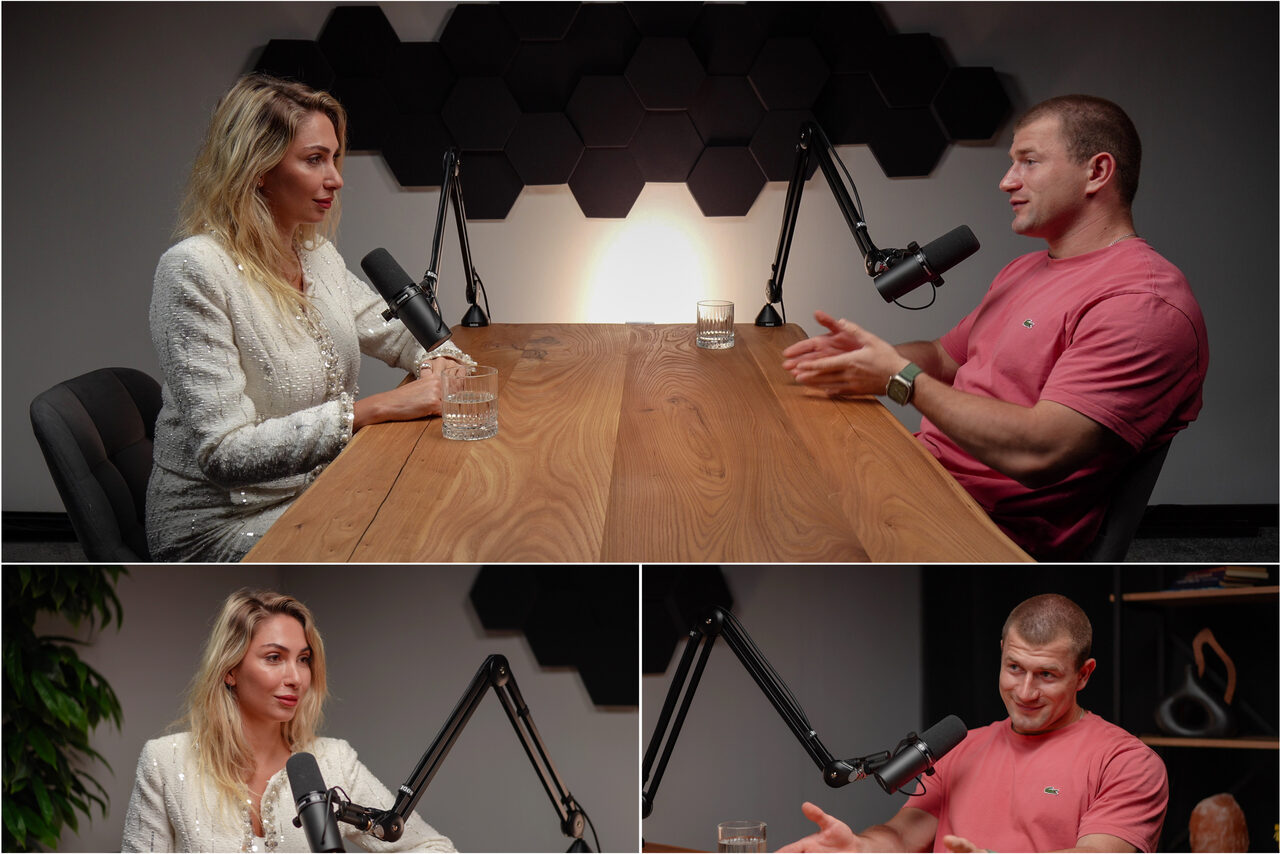 Арендовать Лофт Позитив. Современная студия с деревянным столом и двумя стульями. На столе микрофоны на стойках, стаканы с водой. Стены украшены черными шестиугольными панелями. Используется направленное освещение. Цветовая гамма серая и черная.