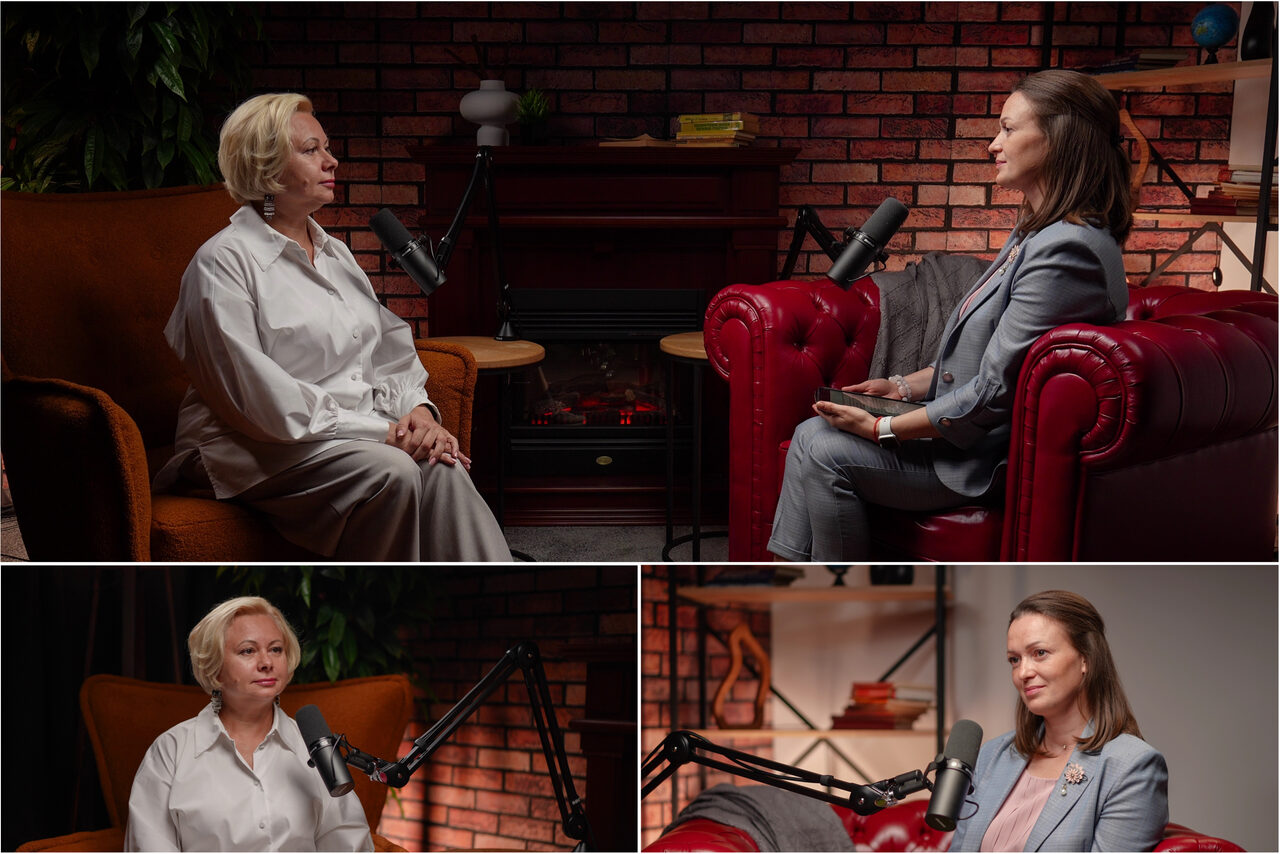 Арендовать Лофт Позитив. Две женщины в студийном пространстве для записей, сидят на коричневом и красном кожаных креслах у кирпичной стены с электрокамином. Есть микрофоны на стойках, растения, полки с книгами и декором. Освещение теплое, мягкое.