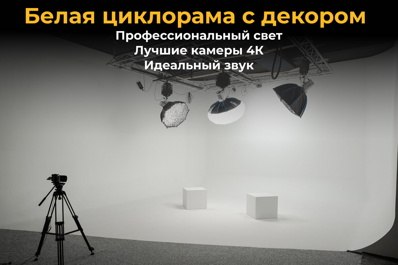 Арендовать Лофт Циклорама. Студийное пространство с белой циклорамой. Две белые кубические тумбы на полу. Осветительное оборудование на подвесной конструкции. Чёрный штатив для камеры. Текст: "Белая циклорама с декором. Профессиональный свет. Лучшие камеры 4К. Идеальный звук".
