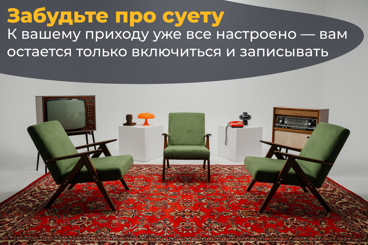 Арендовать Лофт Циклорама. Помещение с тремя зелеными креслами на красном ковре с узором. Слева старый телевизор, справа радио на тумбе. На белых подставках лампа и статуэтка. Яркое верхнее освещение. На серой стене текст: «Забудьте про суету...».