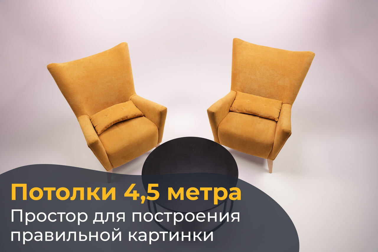 Арендовать Лофт Циклорама. Два оранжевых кресла с подушками расположены вокруг круглого черного стола на белом фоне. Верхняя часть изображения содержит текст: «Потолки 4,5 метра. Простор для построения правильной картинки».