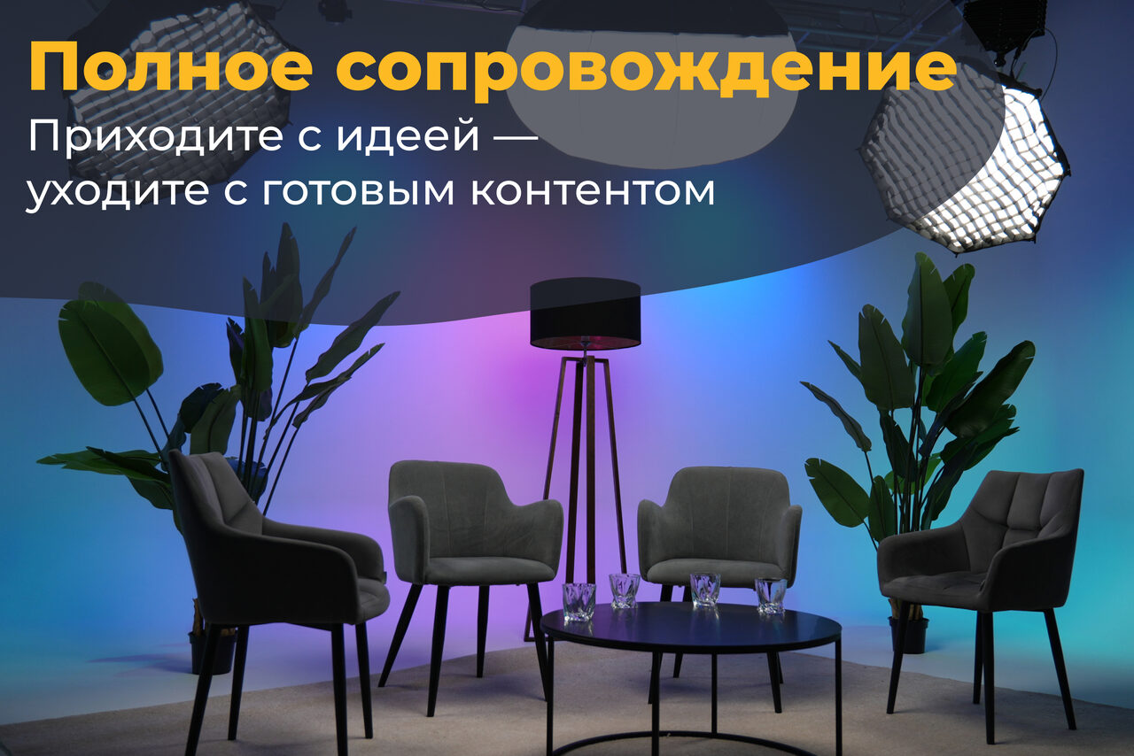 Арендовать Лофт Циклорама. Современное студийное пространство с четырьмя серыми креслами и круглым столиком на сером ковре, окружённое растениями. Зонтичные светильники сверху. Цветная подсветка стен в фиолетовых и синих тонах. Текст на русском о "полном сопровождении".