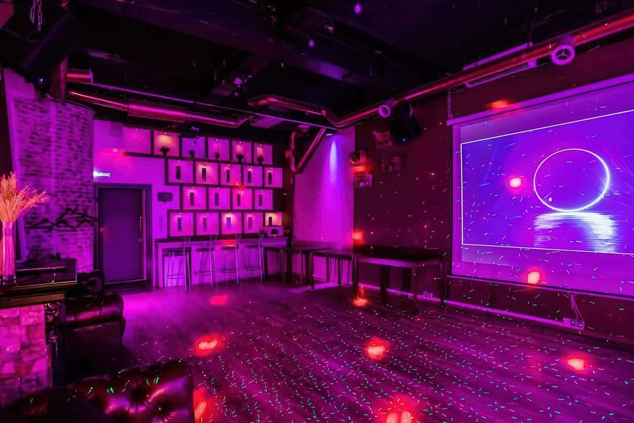 Арендовать LoftForParty. Бэкстейдж лофт . Ночное клубное пространство с танцполом. Проектор демонстрирует неоновое изображение. Стены темные с декоративными элементами и подсветкой. Барная стойка с высокими стульями. Пол под деревянную текстуру. Диваны у стен. Пурпурное и розовое освещение.