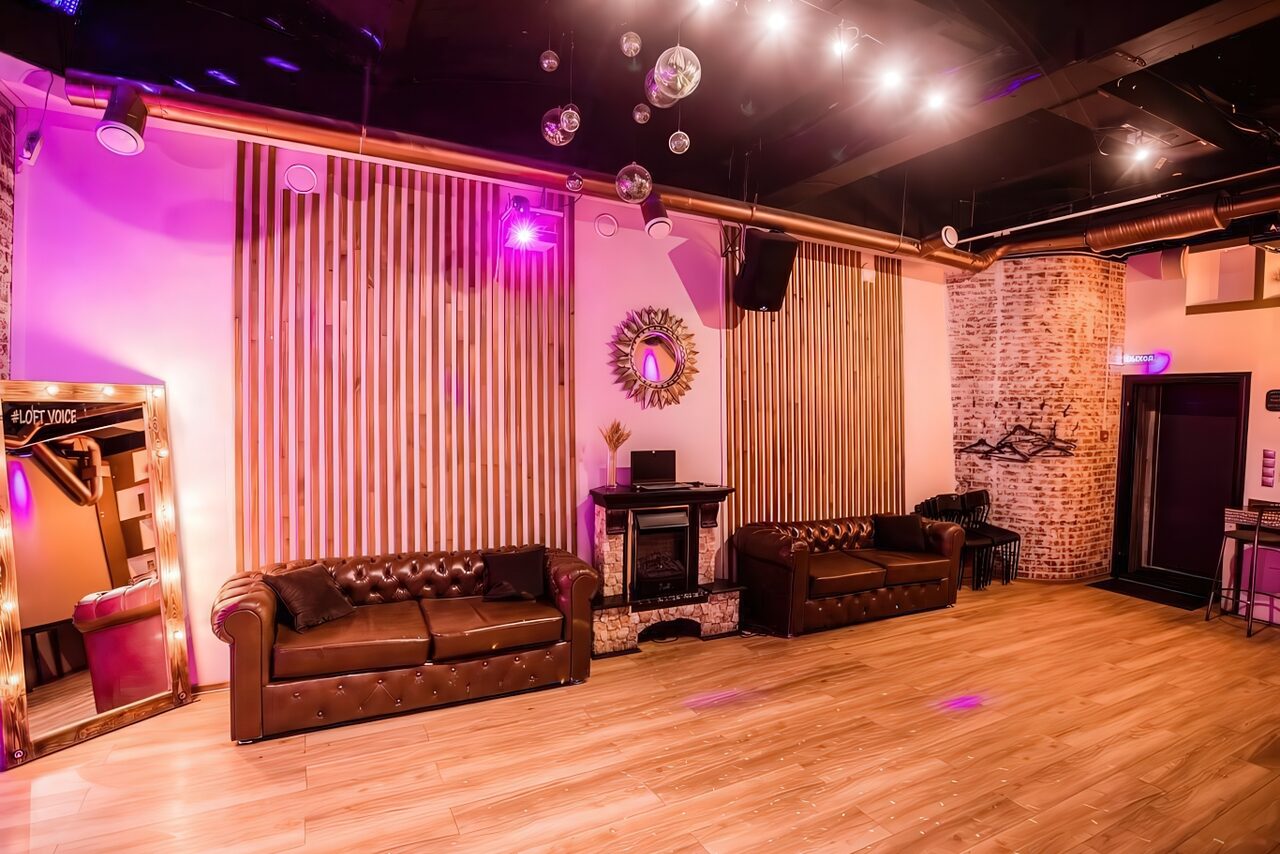 Арендовать LoftForParty. Бэкстейдж лофт . Просторное помещение с деревянным полом и кирпичной стеной. Два кожаных дивана, зеркало, декоративный камин. Потолочные светильники и неоновое освещение. Подвесные шары на потолке. Стены украшены деревянными панелями и круглым зеркалом.