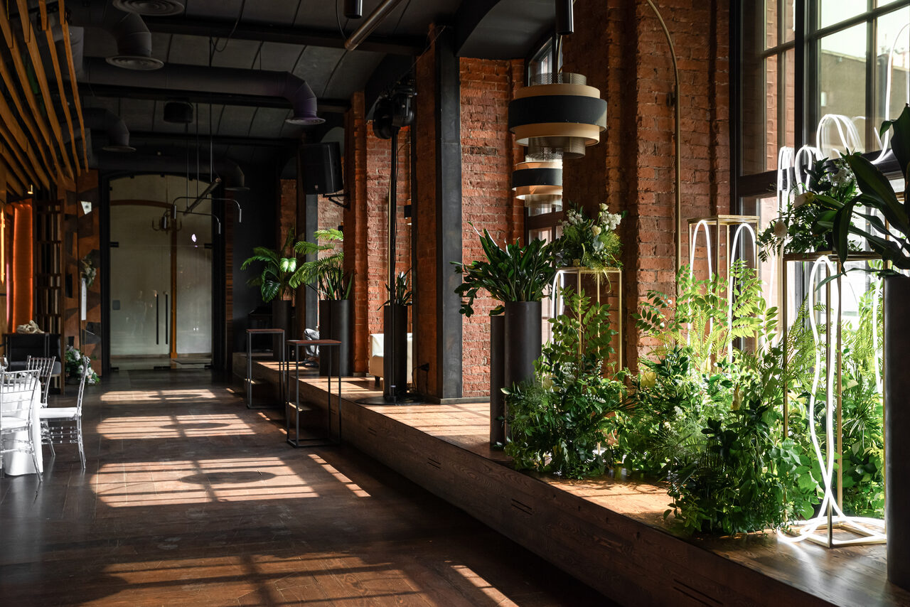 Арендовать Zafferano Loft(Зафферано лофт). Лофт-пространство с кирпичными стенами и большими окнами. Темный потолок с открытыми коммуникациями. Деревянный пол и подиум с растениями. Металлические конструкции, светильники подвесные. Естественное освещение. Стулья и столы из прозрачного пластика.