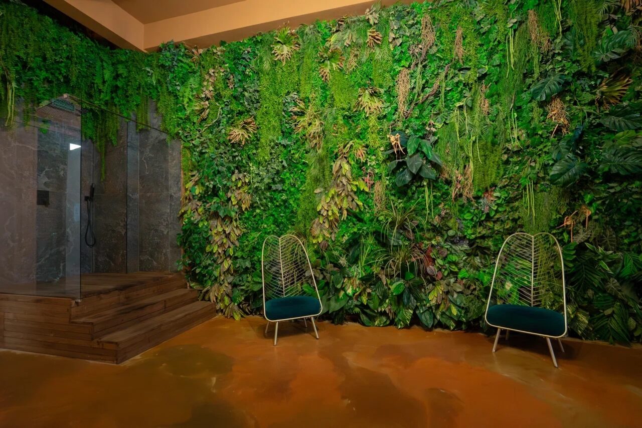Арендовать Polygon(Полигон). Зал Марокко. Стена с живыми растениями, две стальные кресла с зелеными подушками, пол коричневого цвета, душевая кабина с прозрачными стеклами и мраморными стенами, деревянные ступени.