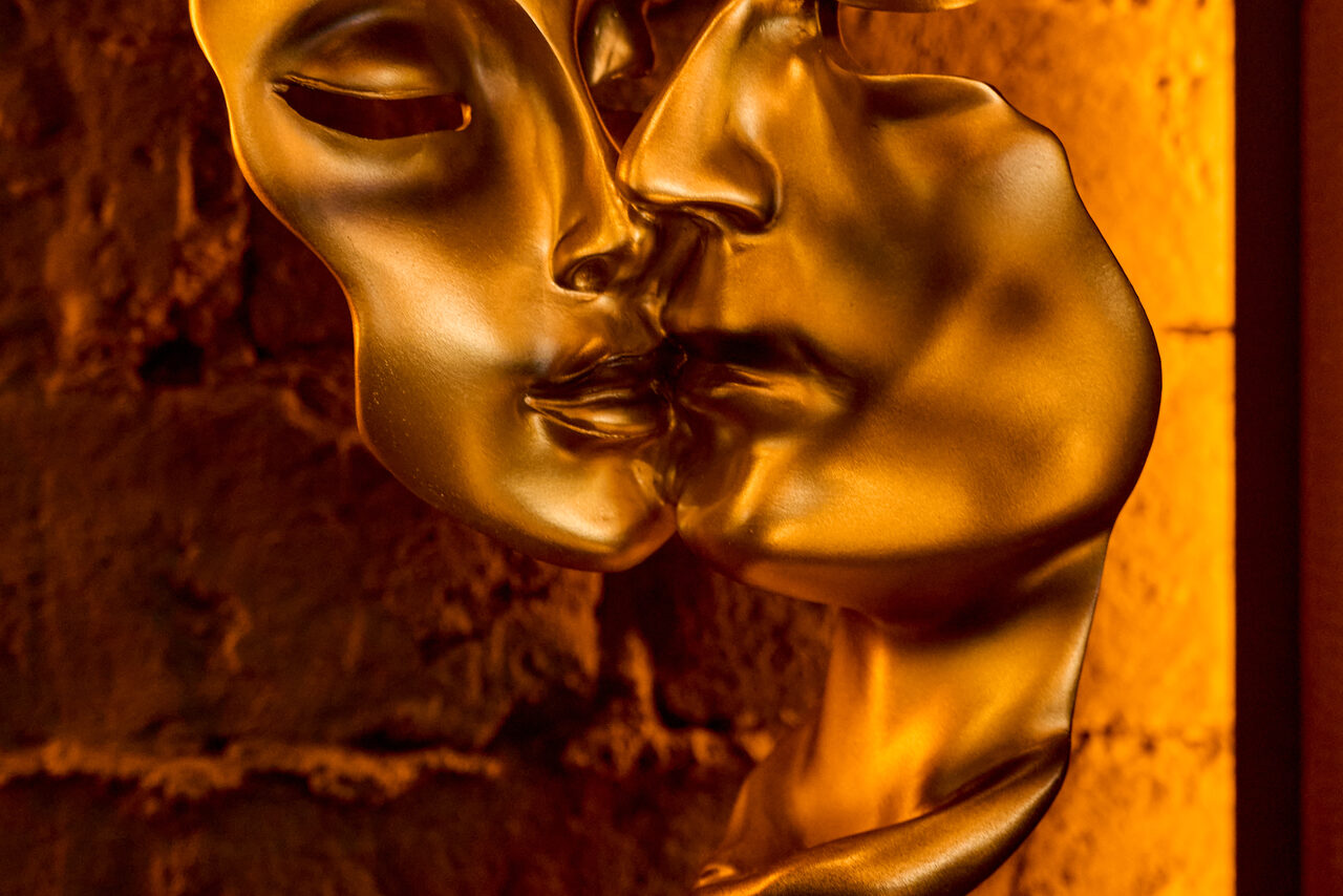 Арендовать Tangiers Lounge(Танжер Лаундж) . Золотистая скульптура двух сливающихся лиц на фоне кирпичной стены, освещенная теплым светом.