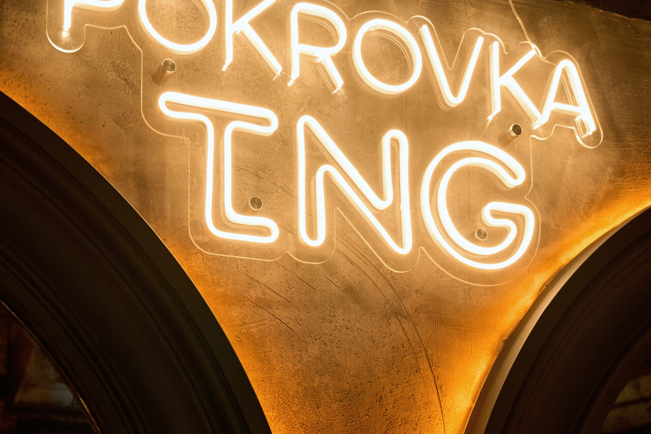 Арендовать Tangiers Lounge(Танжер Лаундж) . Неоновая вывеска с надписью "POKROVKA ING" на бежевой стене. Подсветка создает теплый свет. Слева видна часть темной арки. Стена с видимой текстурой и оттенками коричневого.