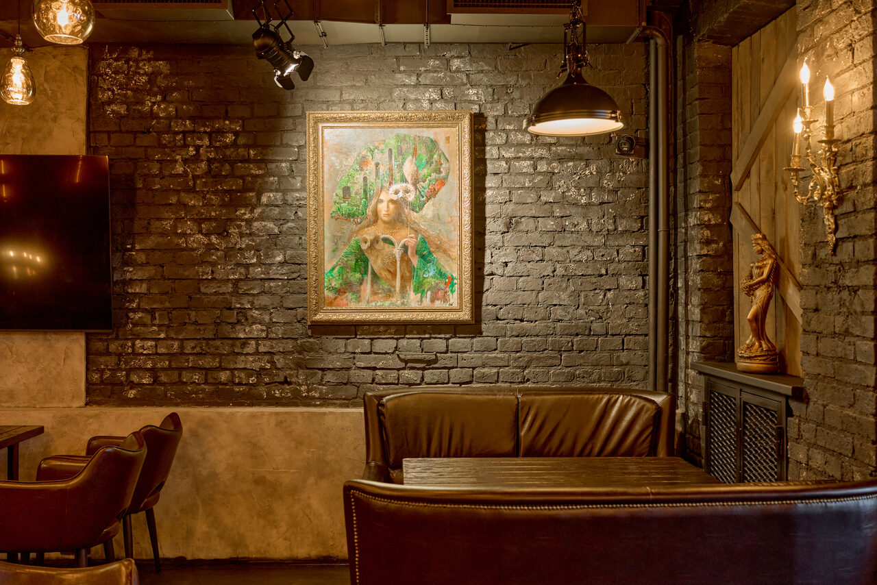 Арендовать Tangiers Lounge(Танжер Лаундж) . Стены из темного кирпича, деревянный стол, кожаные диваны, картина в рамке на стене, потолочные светильники, настенные бра, деревянные панели, декоративная статуэтка, теплое освещение, металлический радиатор.