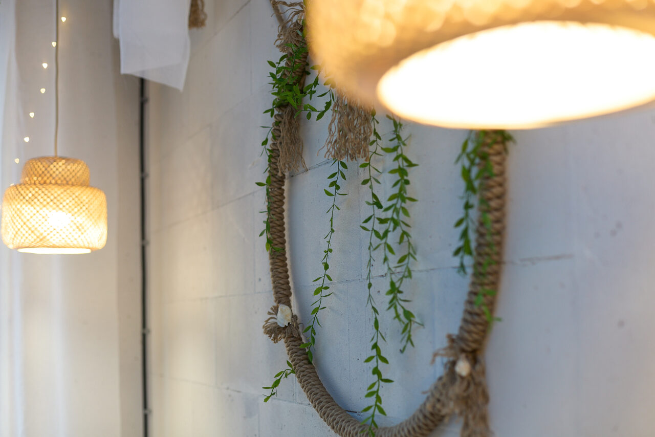 Арендовать Лофт Бали с фото зоной на 23 этаже с видом на Москва-реку. Подвесные светильники с плетёными абажурами, украшение на стене из веревки и зелени, белая стена.