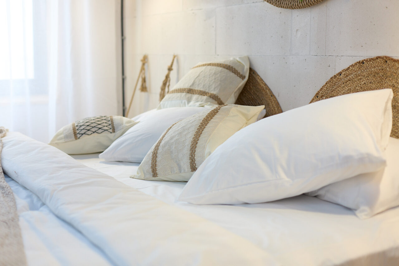 Арендовать Лофт Бали с фото зоной на 23 этаже с видом на Москва-реку. Кровать с белым постельным бельем и мягкими подушками с декоративными элементами. Светлая комната, белая стена, большое окно справа, пропуская естественный свет. Декоративные элементы из натуральных материалов.