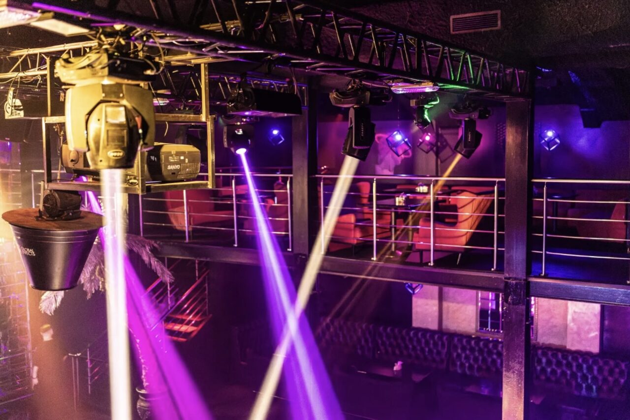 Арендовать Castle Concert Hall(Концертный зал Замок). Клубное пространство с балконом, оборудованное софитами и прожекторами. Диваны красного цвета вдоль стен, металлические перила на втором уровне. Многоцветное освещение, включая фиолетовые и розовые лучи. Потолочные конструкции и сцена.