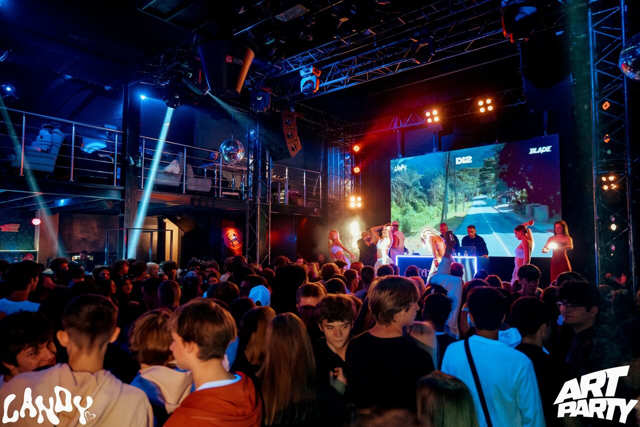 Арендовать Castle Concert Hall(Концертный зал Замок). Большое внутреннее пространство с танцполом, сцена с диджеем и танцорами, светодиодные панели, металлические конструкции. Многоуровневый потолок, красочные световые эффекты, плотная толпа людей. Надписи: «LAVXX», «D2D», «BLAZE», «ART PARTY».