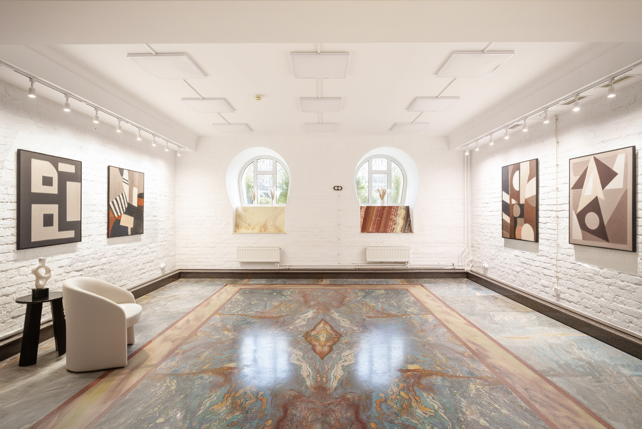 Арендовать Светлый Лофт. Яркое галерейное пространство с белыми кирпичными стенами, мраморным полом, двумя арочными окнами, несколькими абстрактными картинами на стенах, белым креслом и круглым черным столиком. Потолочное точечное освещение.