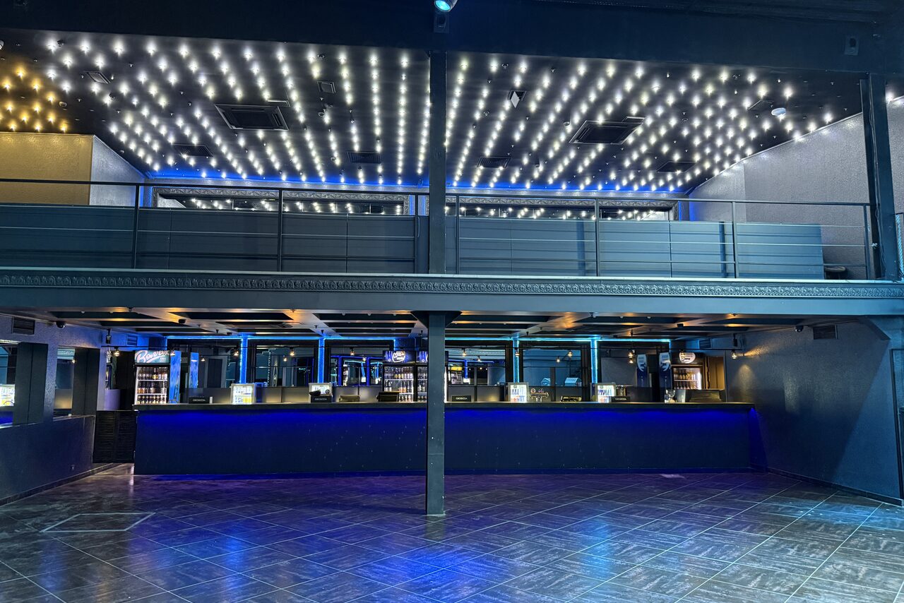 Арендовать СВОБОДА. Зал на 1200 человек. Двухуровневое пространство с дизайнерским потолком, украшенным светодиодами. Открытая планировка. Нижний этаж с просторной барной стойкой, подсвеченной неоновым светом. Стены и потолок синие и черные. Пол покрыт кафелем.