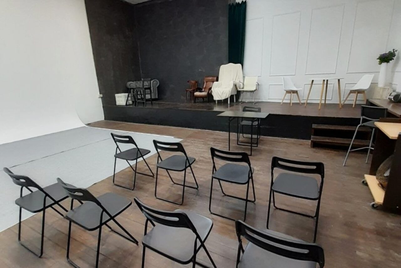 Арендовать Интер-Фото. Студийное пространство с деревянными полами, черная стена, белый циклом. Стулья в два ряда, кресла на подиуме. Столы, растения на подоконнике. Светлый и темный текстиль, панели на стене.