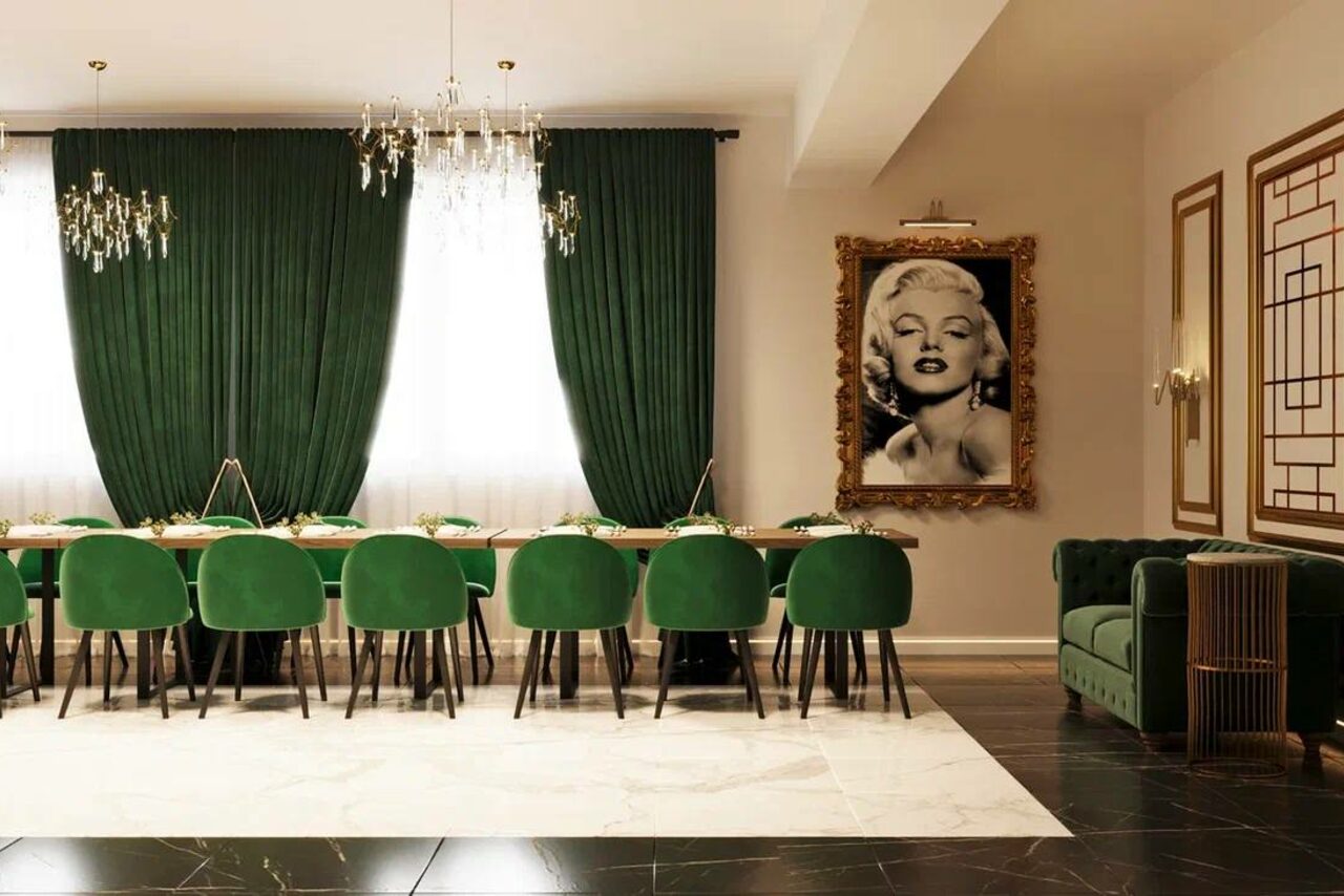 Арендовать Голливуд. Элегантный лофт в зелено-бежевых оттенках. Столовая с длинным деревянным столом и десятью зелёными стульями, зелёные шторы на окнах, два подвесных светильника, черно-белое фото в позолоченной раме, зелёный диван в углу, светлые стены, пол из светлого мрамора и тёмного гранита.