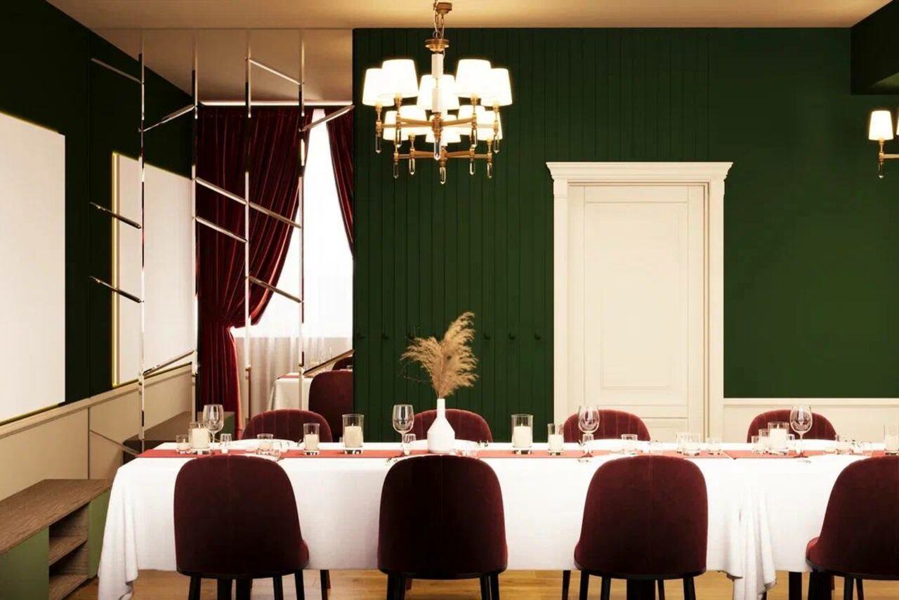 Арендовать Вегас. Атмосферный лофт с акцентным дизайном. Простор с длинным столом, накрытым белой скатертью, окружённый бордовыми стульями. Зеленая стена с белой дверью, золотые люстры, тёмно-красные шторы. Декор на столе из сухих растений в вазе. Светлое деревянное напольное покрытие.