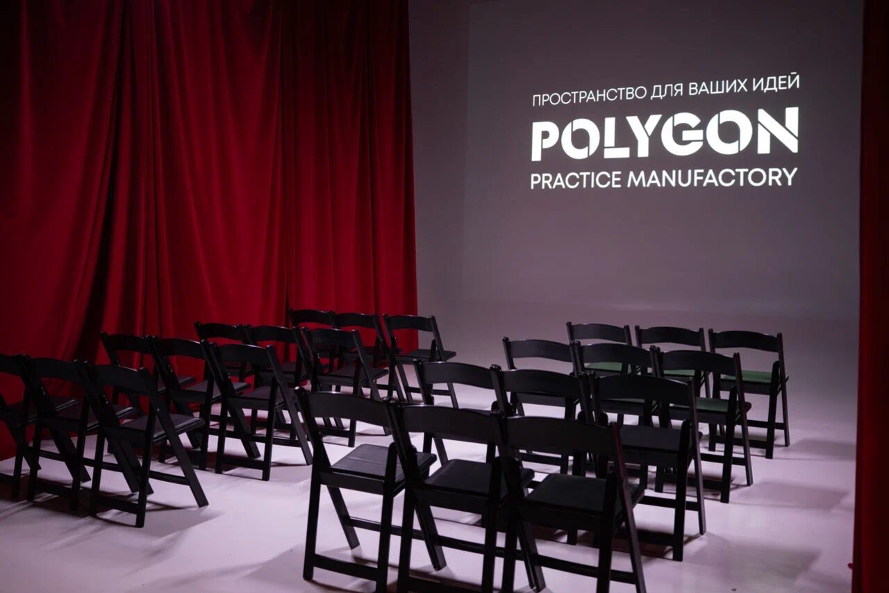 Арендовать Polygon(Полигон). Зал Вышка. Помещение с черными складными стульями в рядах, красными занавесками, белым экраном с логотипом "Polygon Practice Manufactory" и надписью "Пространство для ваших идей". Белый пол, нейтральное освещение.