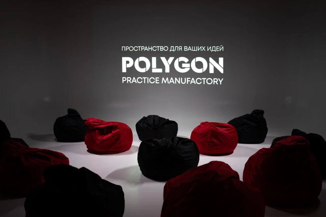 Арендовать Polygon(Полигон). Зал Вышка. Темное помещение с черными и красными креслами-мешками, расположенными по кругу. На стене белая надпись: «Пространство для ваших идей. Polygon Practice Manufactory». Освещение приглушенное, фокус на названии.