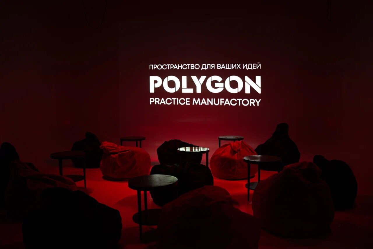 Арендовать Polygon(Полигон). Зал Вышка. Темное пространство с ярким красным освещением. Расставлены кресла-мешки и круглые небольшие столики. На стене надпись: «ПРОСТРАНСТВО ДЛЯ ВАШИХ ИДЕЙ POLYGON PRACTICE MANUFACTORY».