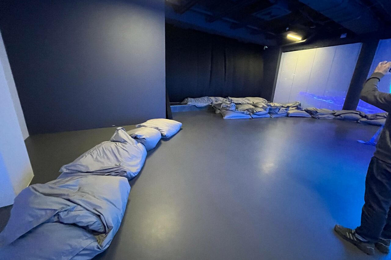 Арендовать Futurione(Футурио́не). Просторное помещение с темными стенами и потолком. По периметру расположены серые сиденья-мешки. Освещение синим светом. Пол темного цвета. Один человек стоит в правой части кадра, частично виден.