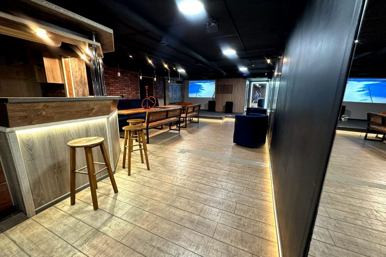 Арендовать BULL LOFT(Лофт Бык) . Лофт-пространство с барной стойкой, деревянными стульями и скамейками. Пол из светлого дерева, стены из кирпича и черного покрытия. Яркое встроенное освещение и проекторы с экранами. Потолок черный. Светлая мебель, теплый свет.