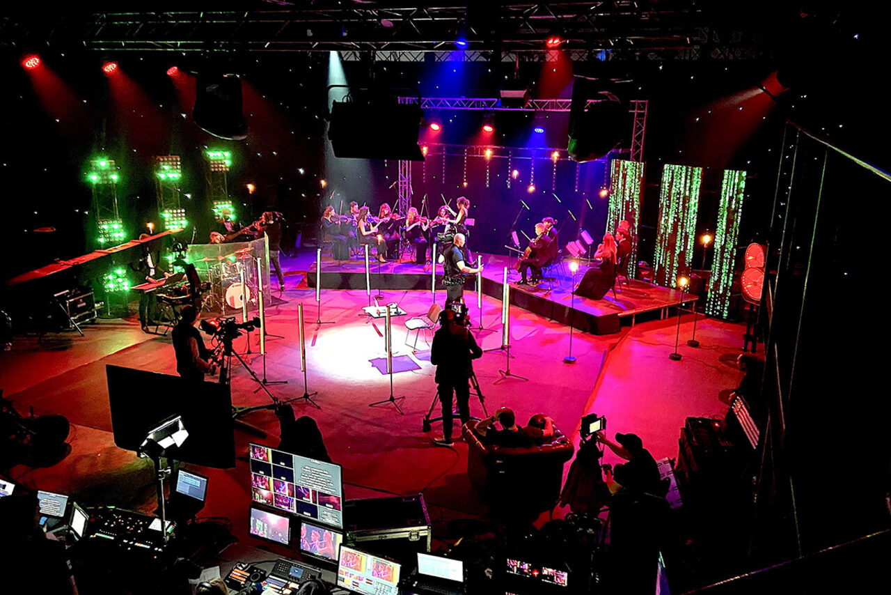 Арендовать Studio Hall(Студио Холл). Концертное пространство с музыкантами на сцене. Вокруг установлены световые приборы, стойки с микрофонами и камеры. Красное, зелёное и фиолетовое освещение. На переднем плане экраны с мониторами. Платформы и ограждения из стекла.