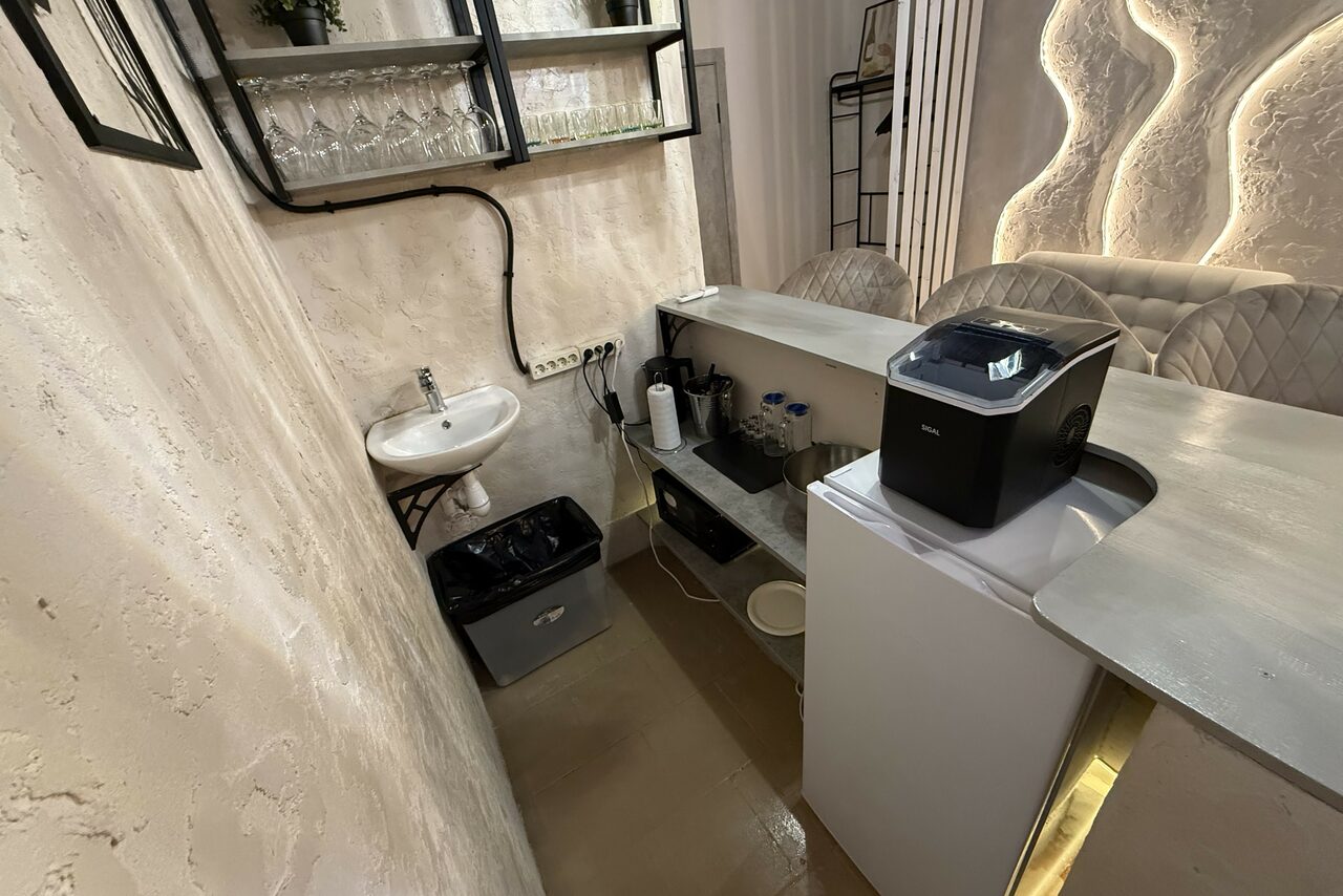 Арендовать Лофт SUNRISE(Восход Солнца). Просторное помещение на 15 гостей. Небольшая зона приготовления с раковиной, открытыми полками со стеклянной посудой, барной стойкой с ледогенератором, закрытыми ящиками. Светлые стены с текстурой, металлический стул, бежевые стены. Освещение с декоративной панелью.