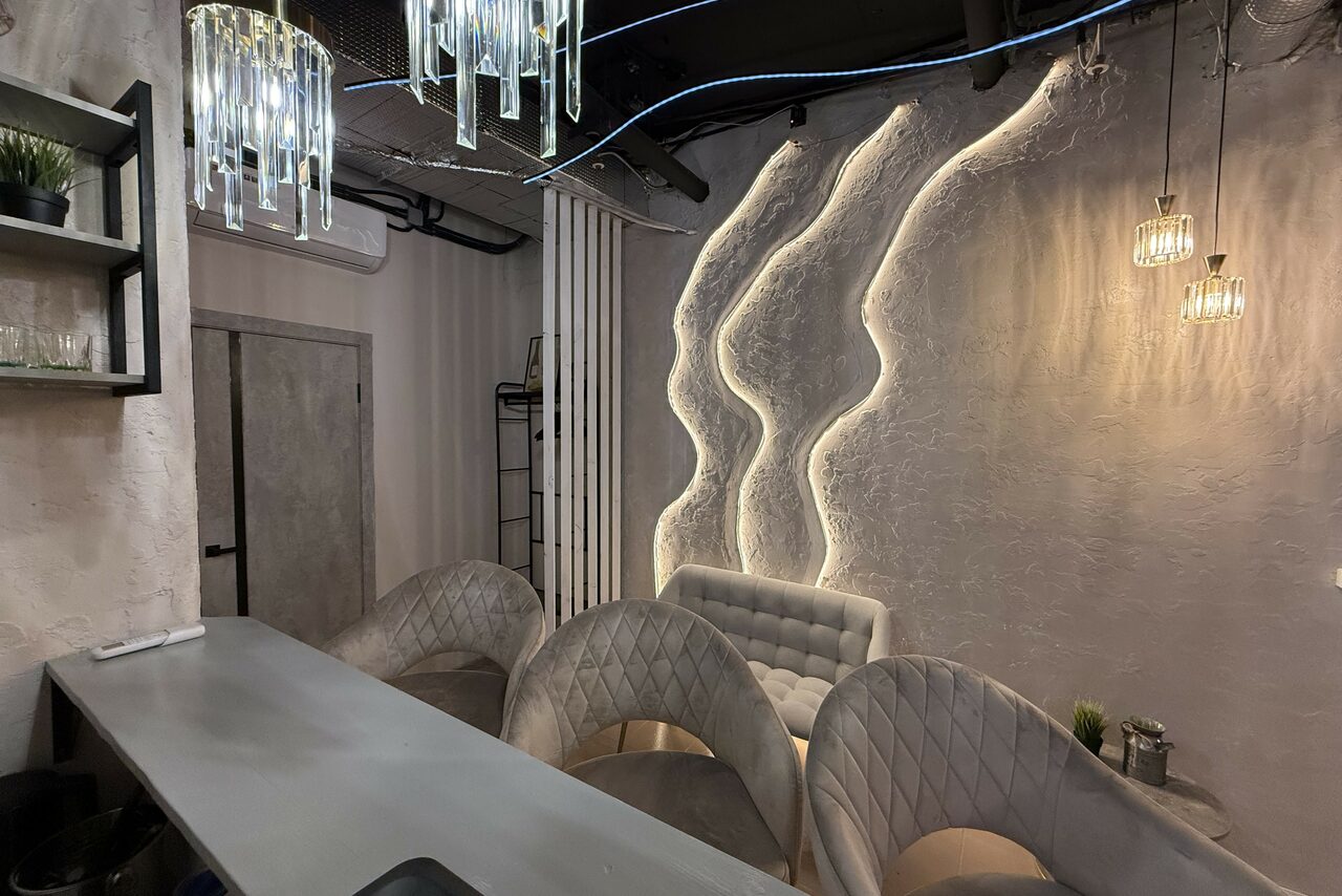 Арендовать Лофт SUNRISE(Восход Солнца). Просторное помещение на 15 гостей. Лофт-пространство с барной стойкой и барными стульями, светло-серая обивка, кованая металлическая стена с подсветкой, мягкое освещение, декоративные подвесные лампы, открытые вентиляционные трубы, полки с растениями.