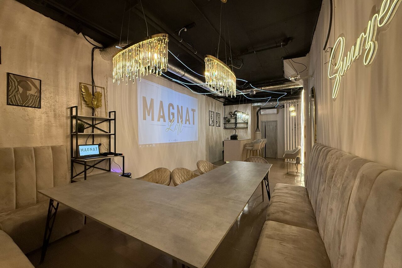 Арендовать Лофт SUNRISE(Восход Солнца). Просторное помещение на 15 гостей. Лофт-пространство с бетонным столом, вокруг которого расположены стулья и мягкие сиденья вдоль стен. Освещение из подвесных светильников, неоновая надпись на стене. Проектор с экраном, металлический стеллаж, декоративные элементы и картины на светлых стенах.