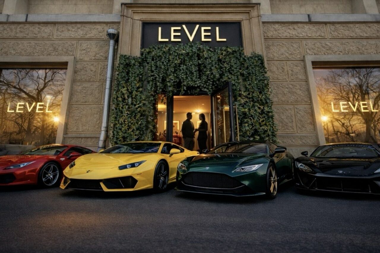 Арендовать Level 5(Лэвел 5). Вид здания с крупными окнами и вывесками "LEVEL", обрамленное растительностью. Перед входом выстроены три спортивных автомобиля красного, жёлтого и зелёного цветов. Внутри видны силуэты людей.