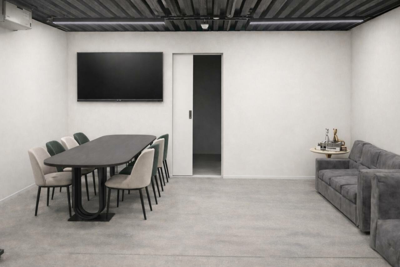 Арендовать Level 5(Лэвел 5). Современная переговорная комната с длинным черным столом и восьми стульями. На стене большой экран. Справа серый диван и небольшой столик с аксессуарами. Светлые стены, пол из светло-серого материала, потолок темный с освещением.