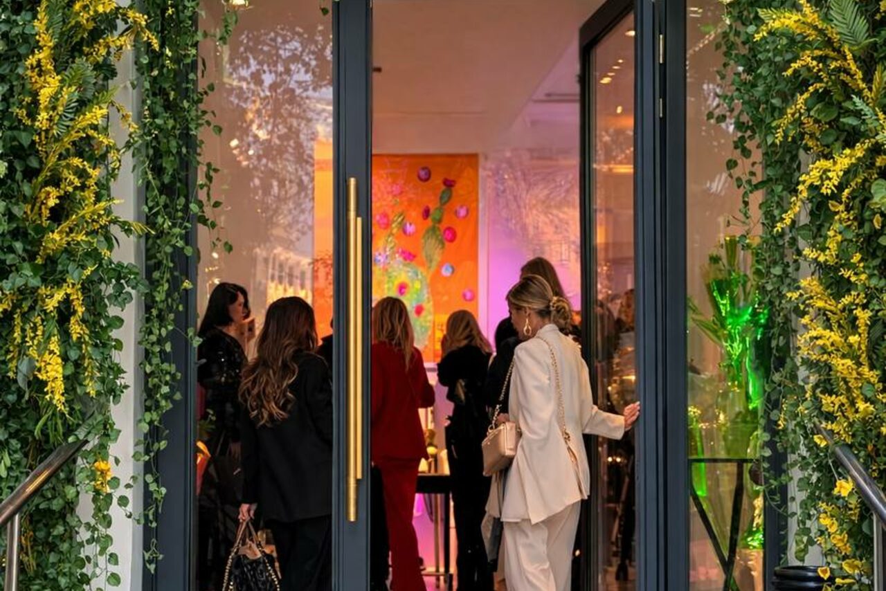 Арендовать Level 5(Лэвел 5). Вход в помещение со стеклянной дверью, украшенной зеленью и жёлтыми цветами. Внутри группы людей, яркое искусственное освещение, на стене видно яркое абстрактное искусство.