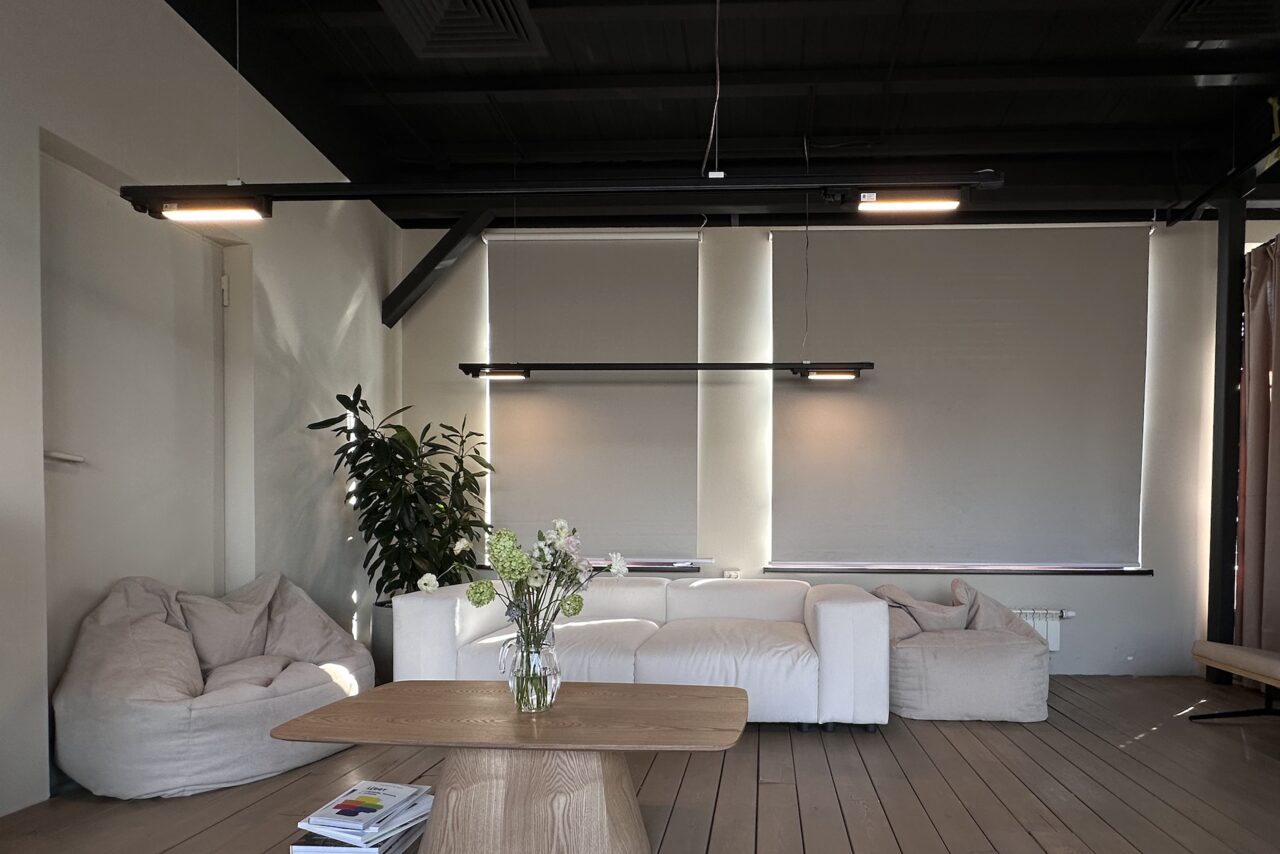 Арендовать Пространство с террасой до 50 человек. Просторная комната с мягким освещением, белым диваном и креслами-мешками. Светлые стены и потолок. Деревянный журнальный стол украшен вазой с цветами. Нейтральные цвета. Растение в горшке возле дивана. Шторы закрывают окна.