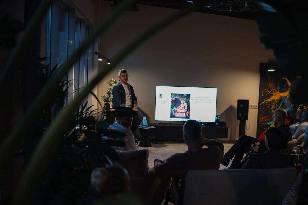 Арендовать Пространство с террасой до 50 человек. Пространство для семинаров: зал с сидячими местами, телевизор на стене, натуральное и искусственное освещение, присутствуют растения, стены в нейтральных тонах, люди сидят и слушают презентацию.