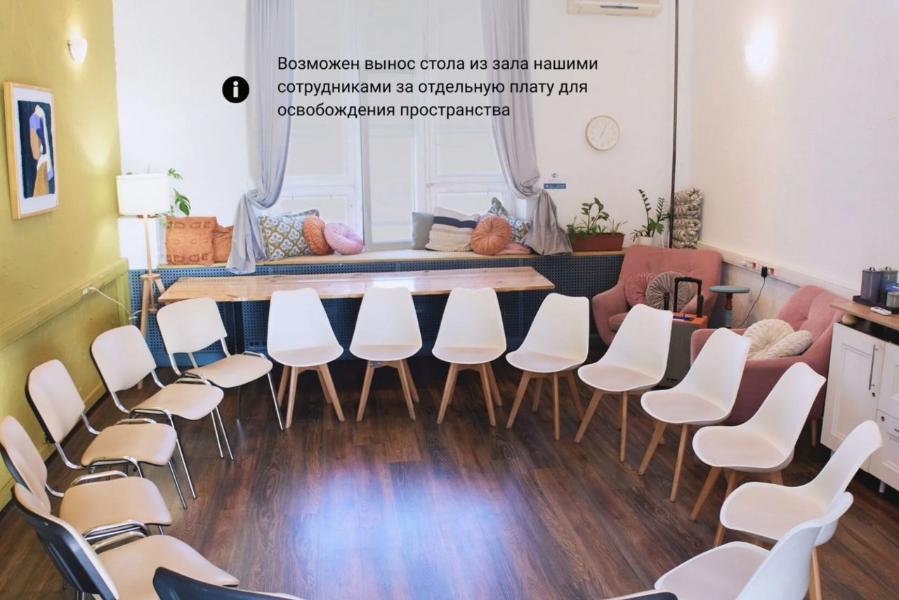 Арендовать H4U. Светлый зал П-602. Просторная светлая комната с круговой расстановкой белых стульев. На деревянном полу расположен стол с подушками у окон. На стене картина и часы. Светлые стены, зелёное кресло, розовый диван, комнатные растения. Вывеска с текстом на русском.