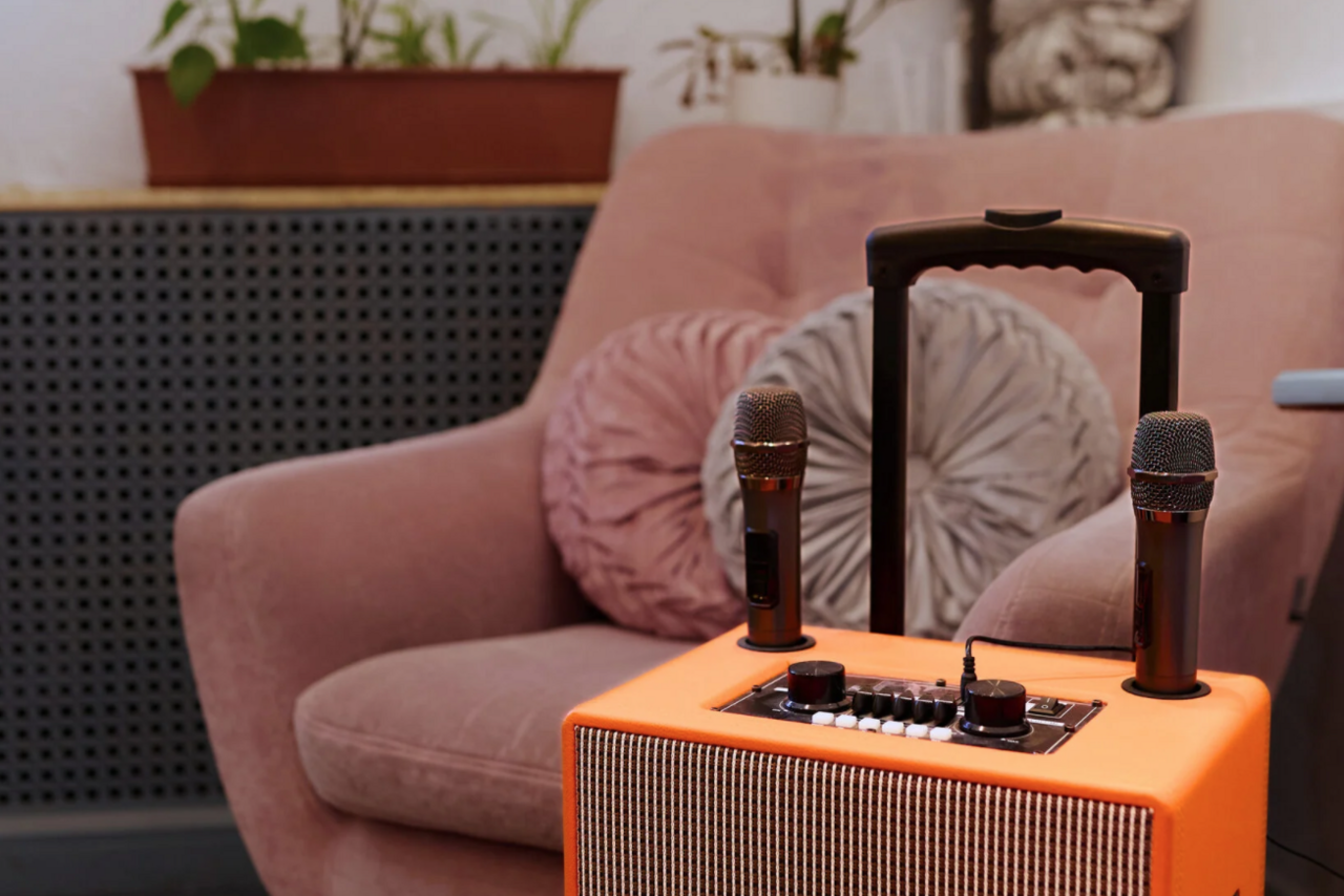 Арендовать H4U. Светлый зал П-602. Мягкое кресло с розовыми подушками, оранжевый усилитель с двумя микрофонами на переднем плане, серый радиатор на заднем фоне, растения на полке.