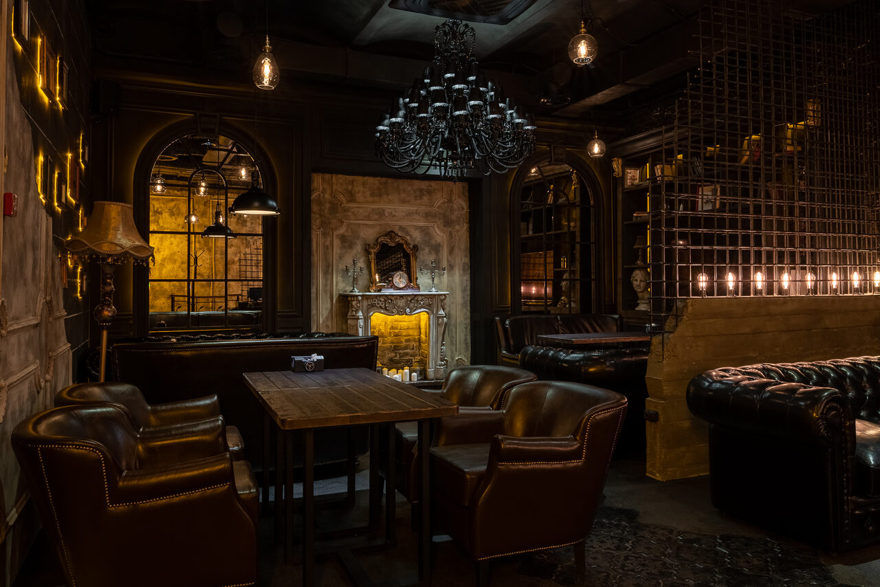 Арендовать Каминный Зал Tangiers lounge Pokrovka(Танжерс Лаундж Покровка). Частное пространство в индустриальном стиле с деревянным столом и кожаными креслами, камином, кожаными диванами, декоративной решеткой, винтажными лампами и люстрой. Оттенки теплые, коричневые и черные. Стены отделаны под кирпич и панели.