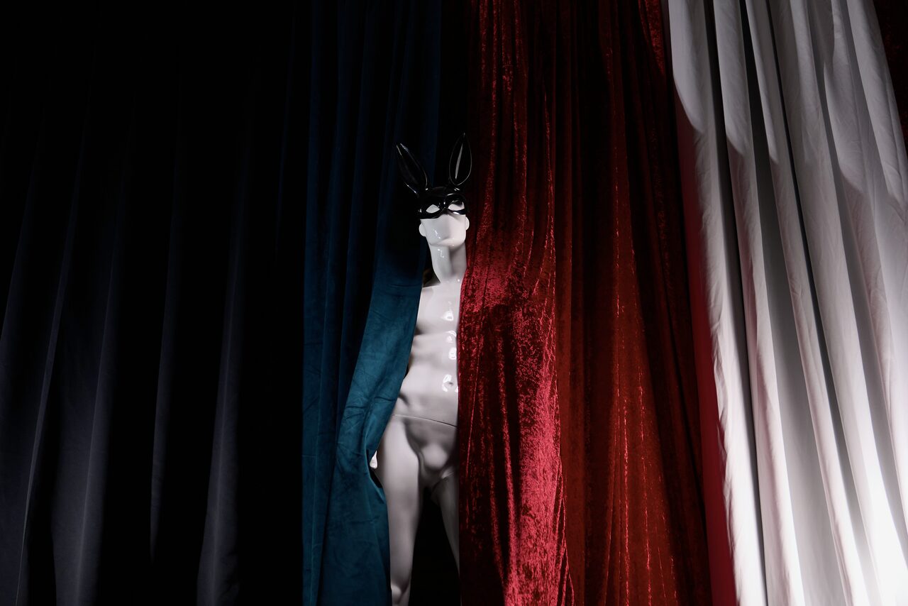 Арендовать WhiteFox Studio(Студия Белая Лиса). Манекен с маской стоит между плотными шторами тёмных и бордовых оттенков. Освещение мягкое, направленное. Текстурированные ткани создают контраст с глянцевой поверхностью манекена.