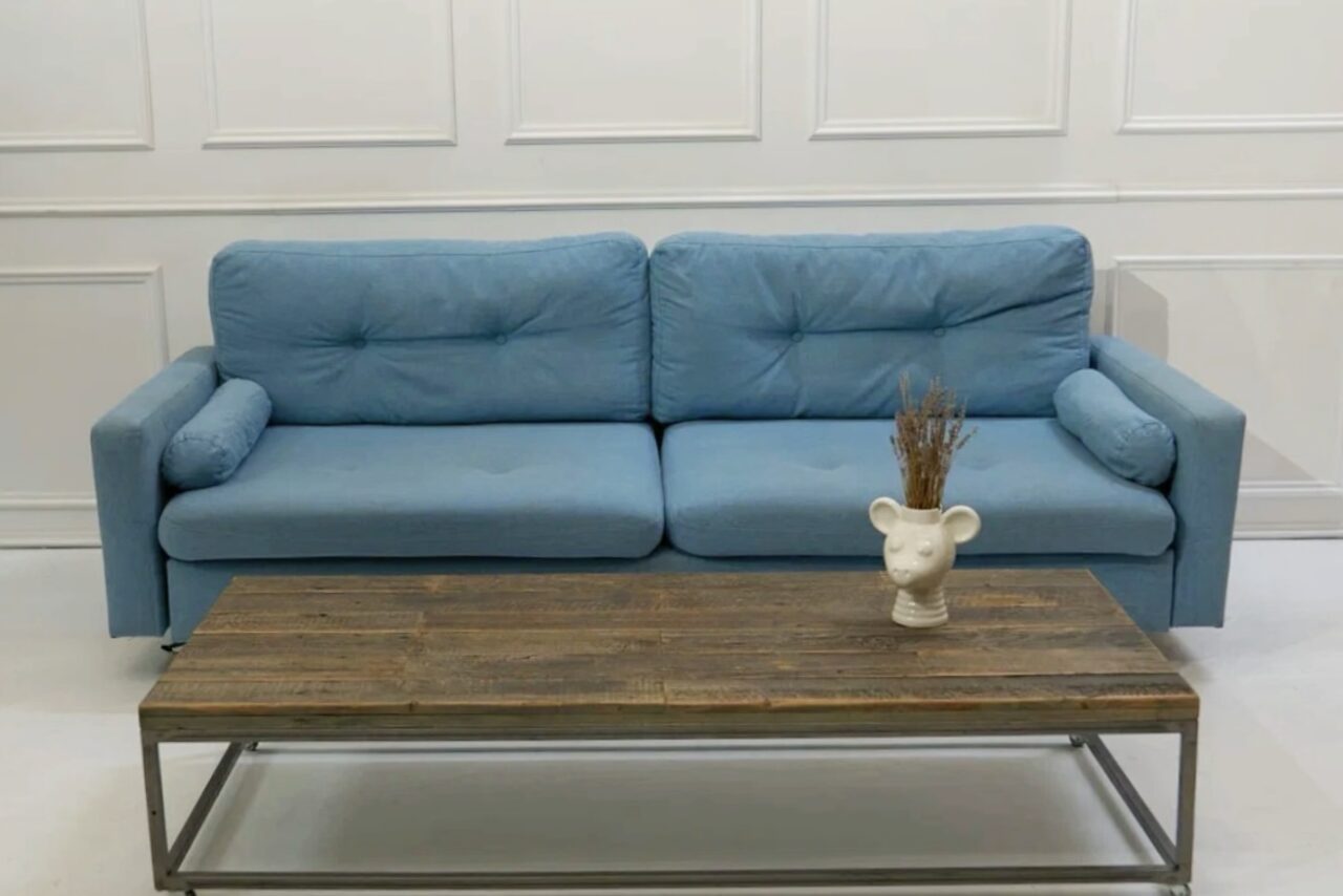 Арендовать WhiteFox Studio(Студия Белая Лиса). Пространство с белыми стенами и голубым диваном. Перед диваном деревянный кофейный стол с металлическими ножками. На столе стоит декоративное изделие в виде головы с сухими растениями. Стиль минималистичный.