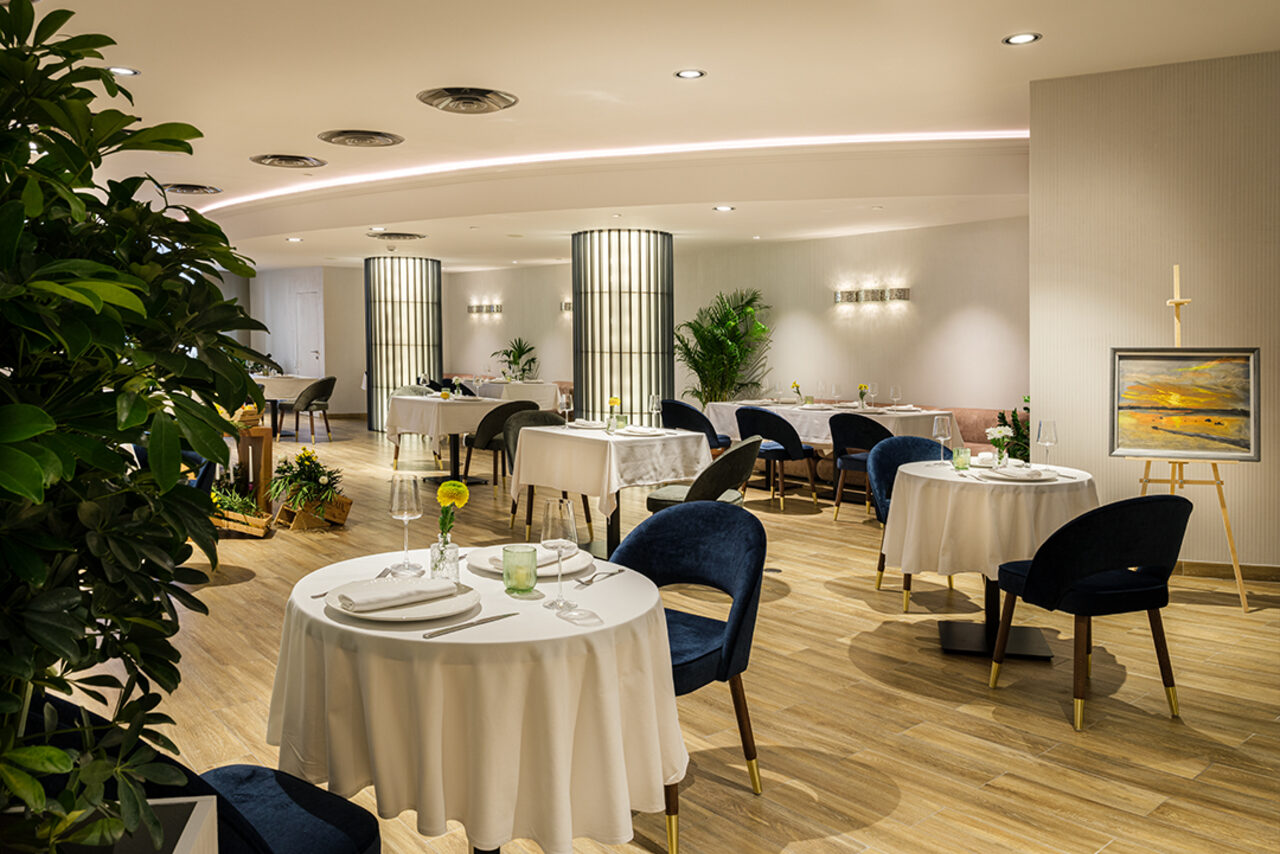 Арендовать Итальянский ресторан Umberto(Умберто). Просторное помещение в стиле ресторана с круглыми столами, покрытыми белыми скатертями. Темно-синие стулья, деревянный пол. Декор из растений и картины на мольберте. Мягкое освещение с настенными светильниками.