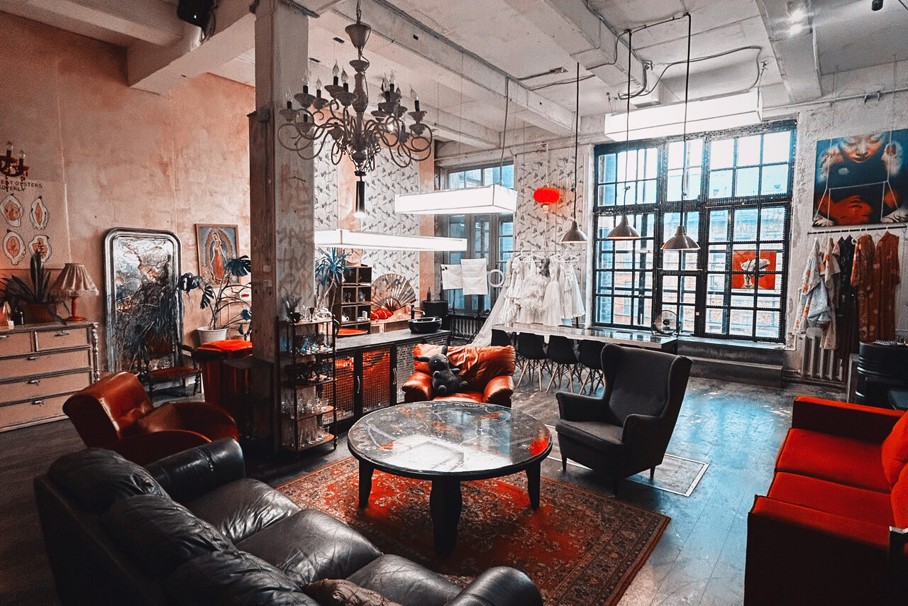 Арендовать Лофт Делюкс. Лофт-пространство с высокими потолками и большими окнами. В центре круглые стеклянные столы, окруженные кожаными креслами и диванами. Присутствуют шкафы, зеркала и декор на стенах. Освещение от разнообразных люстр и подвесных ламп.