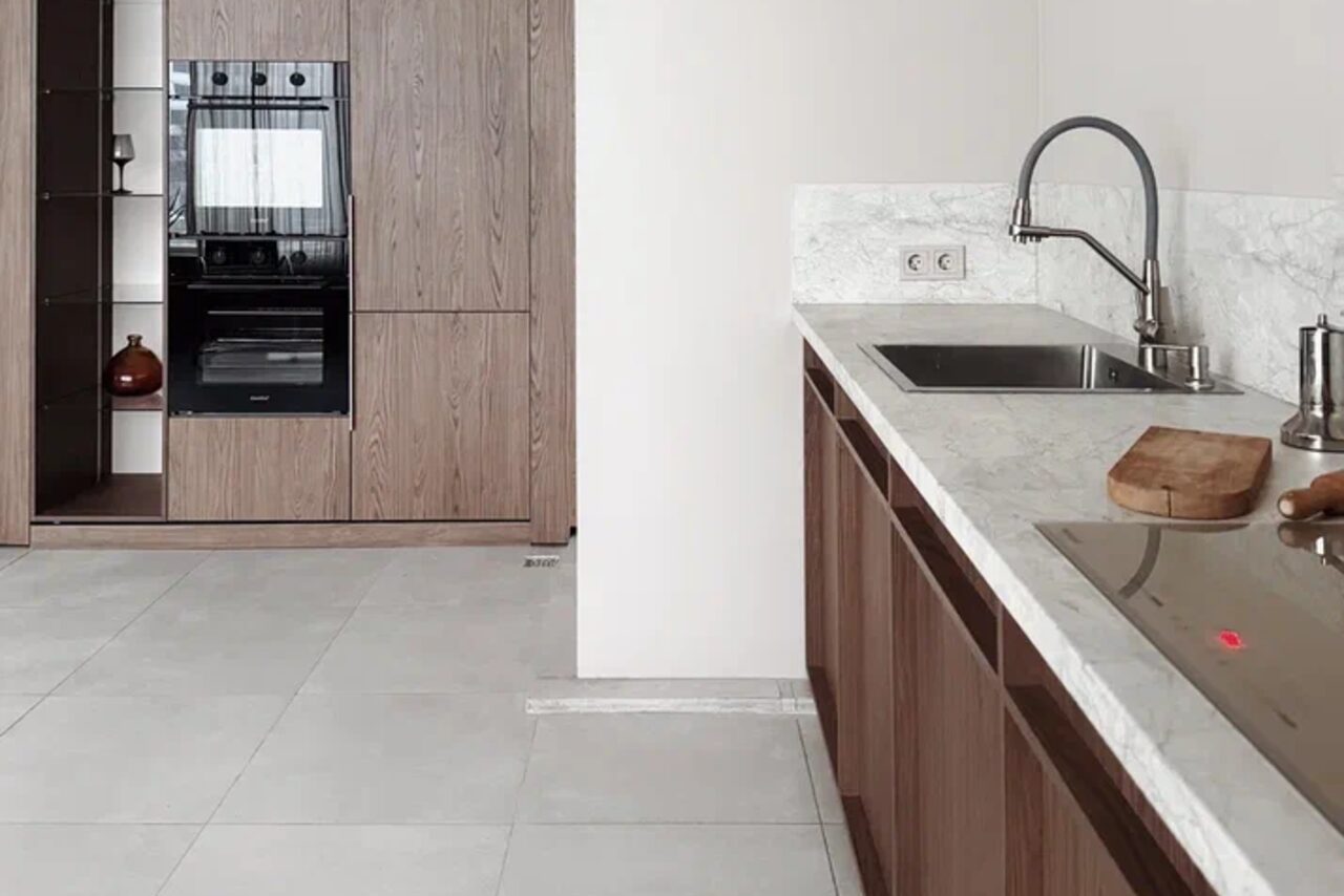 Арендовать Киото. Светлый зал с кухней. Современная кухня с открытой планировкой, деревянные шкафы, встраиваемая техника, белая столешница из камня, металлический смеситель, индукционная варочная панель, плиточный пол, светлые стены, выключатели и розетки на стене.